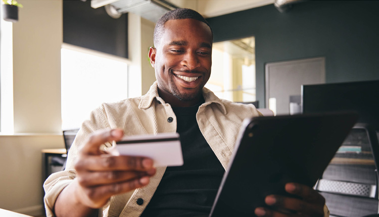 A smiling man holds a debit card and tablet.