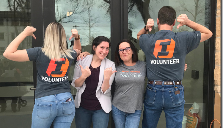 A group of First Interstate volunteers smile as they point to their T-shirts.