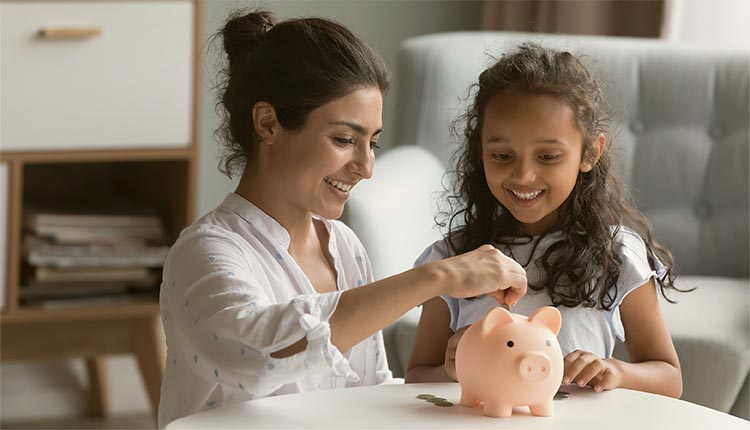 A women and child drop coins into a piggy bank.